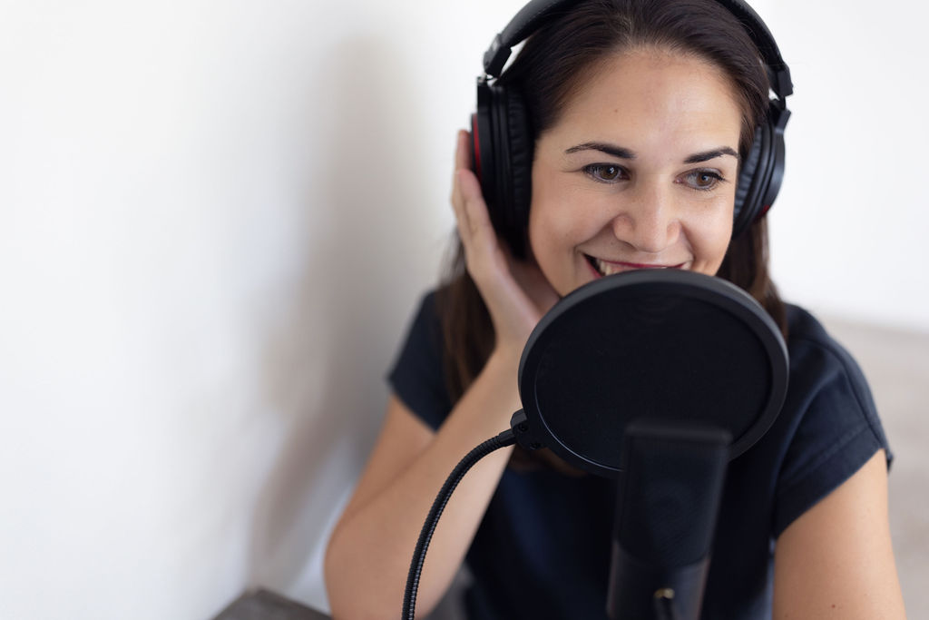 Elena Kersey recording in studio with pop filter in front of microphone and one hand on headphones